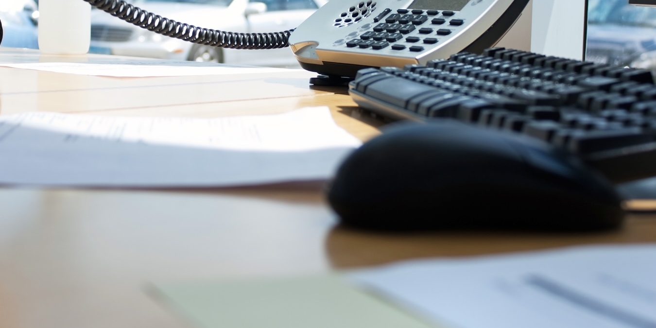 A reception desk: telephone handset off the hook, keyboard and documents on the desk.