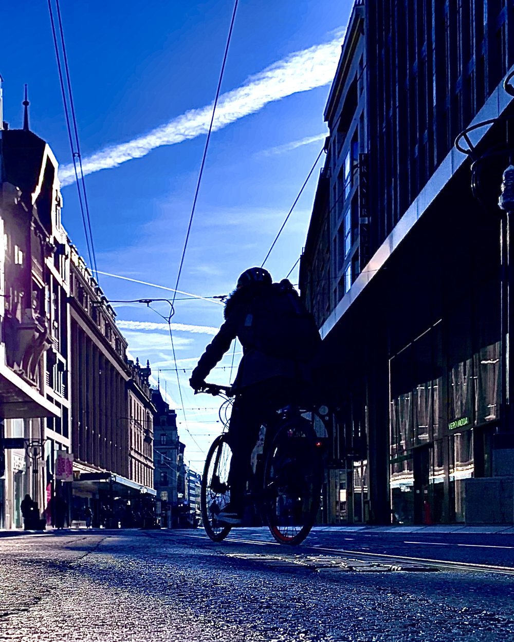 A street in central Geneva at dawn, a cyclist backlit beneath the tram wires.
